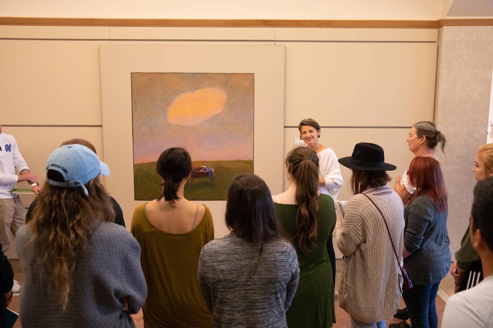 Alexa Miller stands next to a painting, &#8216;Floating Bed,&#8217; in the Cook-DeVos Center for Health Sciences and asks nursing, health professions and art students to discuss what they see.